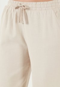 Helle beige weite Hosen aus strukturiertem Stoff mit einem elastischen Bund und Kordelzug sowie seitlichen Taschen.