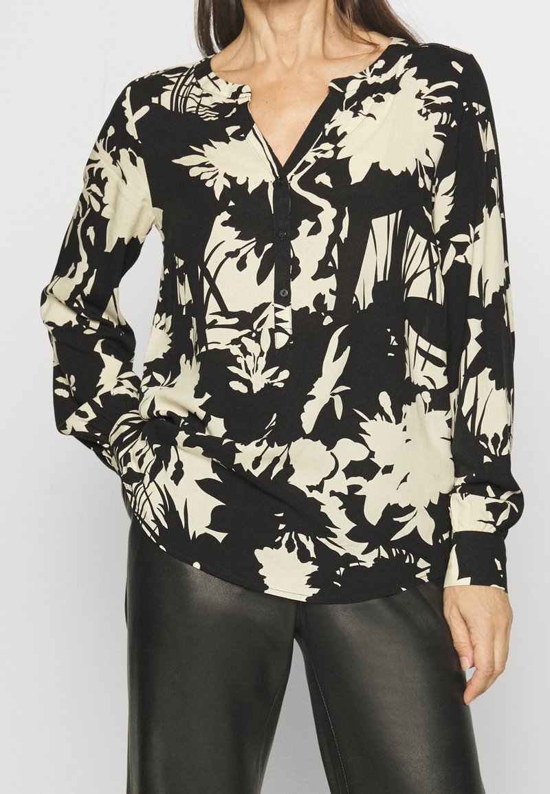 Blouse à manches longues avec un motif floral noir et crème, dotée d'un col et d'une patte de boutonnage. Confectionnée dans un tissu léger avec une coupe décontractée.