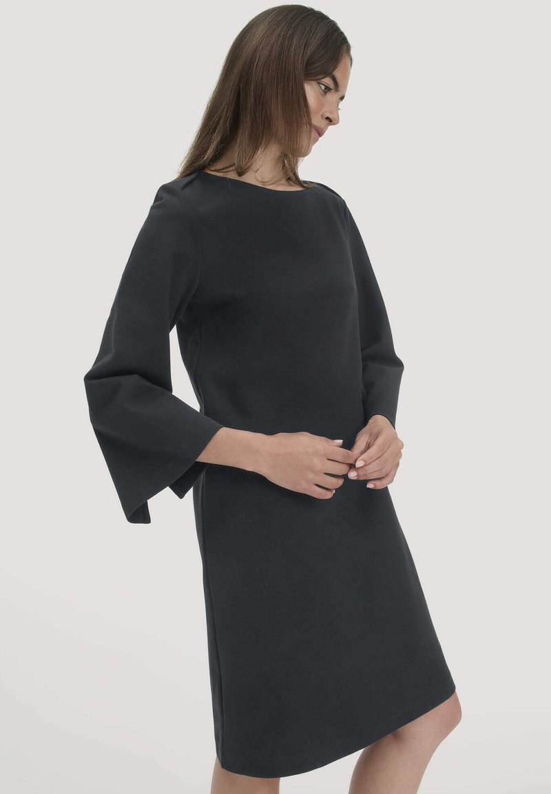 Schwarzes Kleid mit langen, ausgestellten Ärmeln und Rundhalsausschnitt. Der Stoff wirkt glatt mit einem leicht strukturierten Schnitt und knielangem Design.