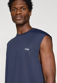 Mornarska brezrokavna športna majica, teksturirana tkanina, okrogli izrez, z majhnim belim logotipom na prsih in kontrastnim dizajnom na ramenih.