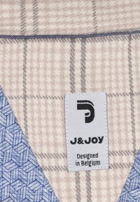 Gekraagde kledingstuk met een zachte geruite textuur in lichtbeige en grijs, met een blauw geometrisch patroon en een etiket met "J&JOY."
