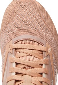 Acercamiento de la puntera de una zapatilla de tela de punto en color salmón, con cordones entrelazados y un diseño de malla transpirable.