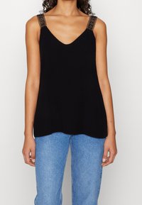 Top nero senza maniche con scollatura a V e spalline in pizzo decorativo; texture liscia con una vestibilità comoda, abbinato a jeans in denim blu chiaro.