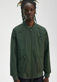 Giacca bomber verde oliva con zip frontale, due tasche con zip e polsini a coste. Realizzata in materiale leggero con una finitura testurizzata.