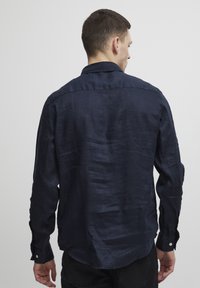 Camisa de manga larga azul marino de lino con acabado texturizado, con cuello abotonado y puños con botones, mostrada desde la parte de atrás.