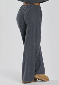 Grå fluffy loungebukser med bred bendesign, elastisk talje og blød tekstur. Bæres med brune støvler, der viser en afslappet pasform.