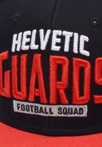 Svart baseballcaps med fet rød og hvit brodert tekst "HEL VETIC GUARDS" og "FOOTBALL SQUAD" på forsiden. Flat bremdesign.