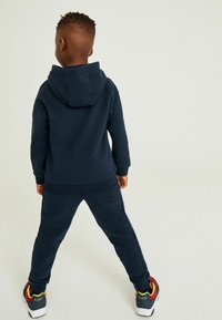 Felpa con cappuccio blu navy e jogger abbinati, in tessuto morbido, vestibilità rilassata, con cappuccio e dettagli testurizzati, abbinati a scarpe da ginnastica multicolori.