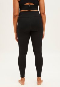 Zwarte hoge taille legging van glad, rekbaar materiaal. Heeft een strakke pasvorm en naadloos ontwerp, geschikt voor sportkleding.