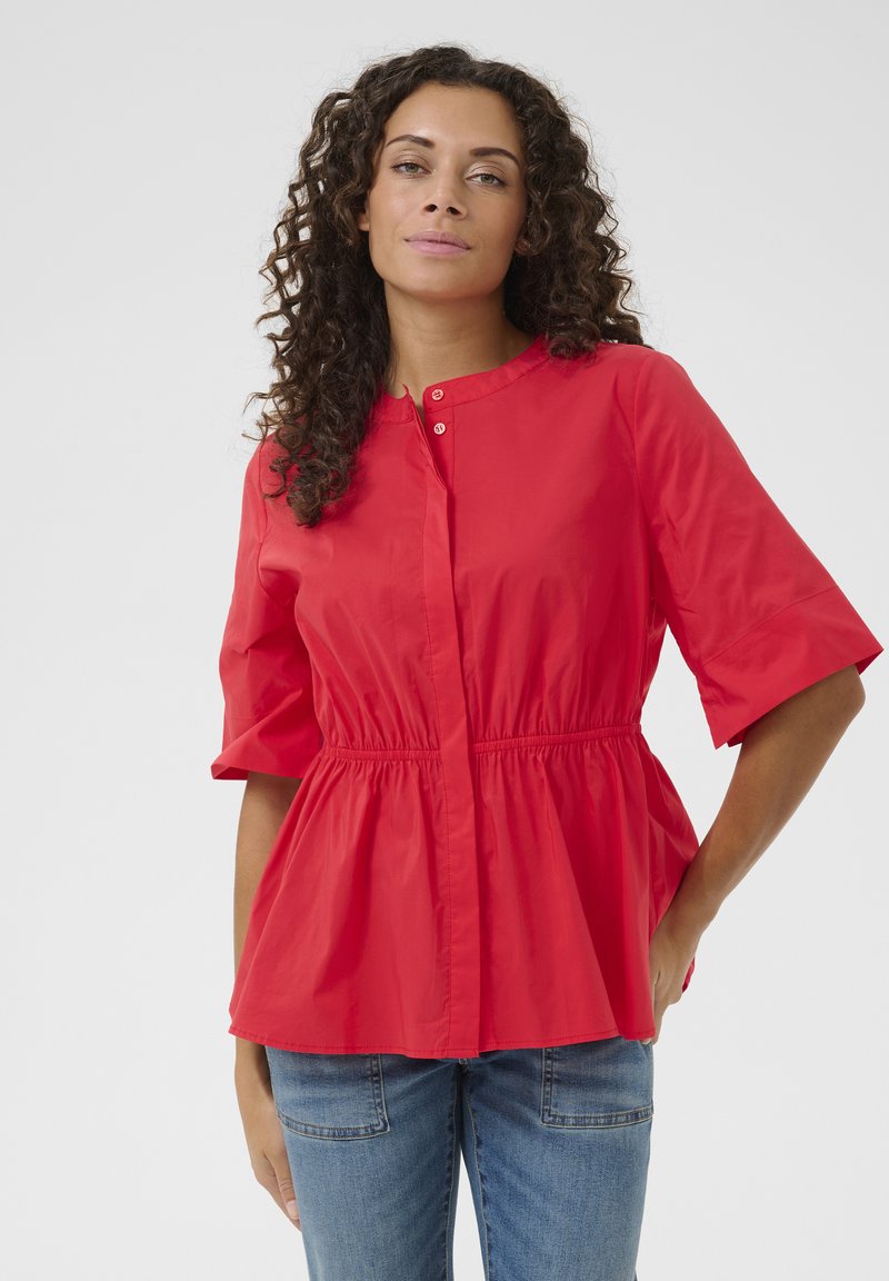 Blusa rossa con maniche corte, vita arricciata e chiusura a bottoni. Realizzata in un tessuto leggero con una consistenza liscia, adatta per un abbigliamento casual.