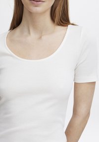 Tricou alb cu dungi, cu decolteu în formă de cerc și mâneci scurte ajustate, având o textură netedă și un design care se mulează pe corp.