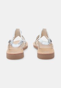 Metallic zilveren sandalen met meerdere dunne banden, een gesp-sluiting en een platte bruine zool. Glad textuur met een minimalistisch ontwerp.