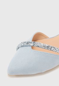 Ballerina in suede azzurro chiaro con punta affusolata, dotata di una fascia decorata con cristalli argentati sulla parte dorsale del piede e un interno nude.