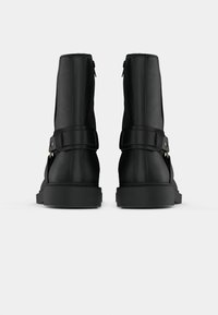 Černé kožené kotníkové boty s hladkým povrchem, s bočním zipem, nastavitelným páskem a plochými gumovými podrážkami.