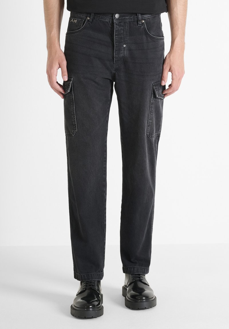 Pantalones cargo de mezclilla negra con corte recto, dos bolsillos laterales y una textura ligeramente descolorida. Combinados con botas negras con cordones.