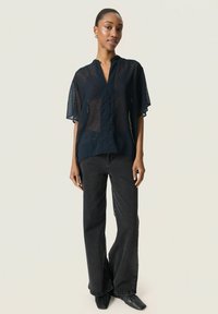 Camicia corta a maniche corte trasparente color navy con scollatura a V e motivo testurizzato, abbinata a jeans neri a vita alta con gamba larga e scarpe nere a punta.