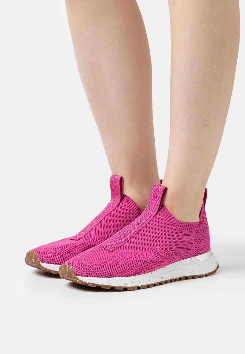 Baskets en maille rose vif à enfiler avec semelles intermédiaires blanches tachetées et semelles extérieures brunes texturées portées pieds nus.