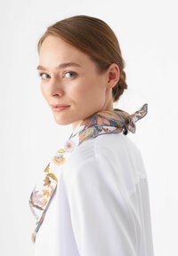 Seidenschal mit floralen Mustern in Pastellfarben, um den Hals gebunden, kombiniert mit einer weißen Bluse, die einen strukturierten Kragen und eine glatte Textur aufweist.
