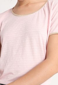 Top de manga corta color rosa claro con cuello redondo y un acento dorado. La tela tiene un suave patrón texturizado.