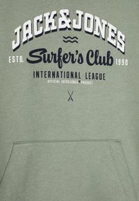 Grön hoodie med en stor tryckt logotyp med texten "JACK&JONES" och "Surfer's Club". Har en framficka och en mjuk tygkänsla.