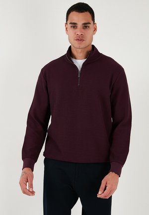 Burgundy, ribbed pullover with a zippered mock neck. Long sleeves and a relaxed fit, paired with a white T-shirt underneath.