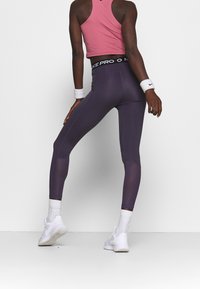 Legginsy sportowe w ciemnofioletowym kolorze z czarnym pasem Nike. Posiadają siateczkowe panele dla lepszej wentylacji oraz gładką, elastyczną teksturę.