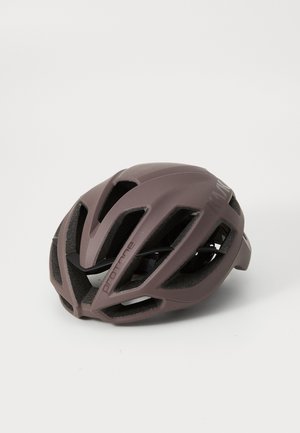 Casque de vélo en mauve mat avec un design aéré, surface lisse et sangles réglables. Présente des lettres audacieuses sur le côté.
