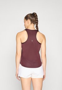 Top deportivo color burdeos con un diseño de malla texturizada, estilo espalda nadadora y detalles de acento sutiles. Combina con pantalones cortos blancos.