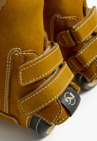 Scarpe gialle in suede con due ampie cinghie in Velcro. Cuciture a contrasto e una suola in gomma nera con un logo sul retro.