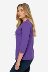 Lila Langarmshirt mit Rundhalsausschnitt, ausgestattet mit einer glatten Textur und figurbetonter Form. Mit Dreiviertelärmeln und geradem Saum gestaltet.