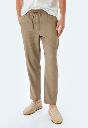 Leichte, beige Leinenhosen mit einem elastischen Kordelzugbund und seitlichen Taschen. Kombiniert mit geflochtenen Slippern.