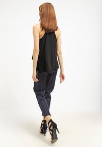 Top nero senza maniche con un design fluido, abbinato a pantaloni a righe blu navy e sandali neri con tacco alto, che mostrano una silhouette elegante.