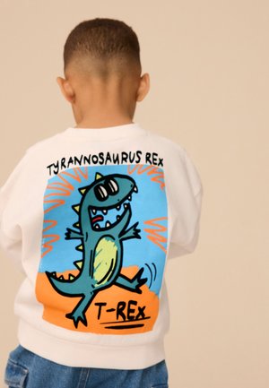 Enfant portant un sweat-shirt blanc avec un T-Rex cartoon coloré et le texte « Tyrannosaurus Rex T-Rex » au dos.