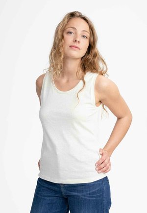 White sleeveless tank top made of cotton, featuring a round neckline and a relaxed fit. Paired with blue denim jeans, displayed against a neutral background.