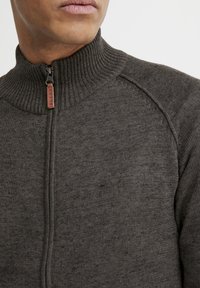 Suéter de punto gris oscuro con un alto cuello de canalé, cierre frontal con cremallera y tejido texturizado. Etiqueta de cuero con acento "BLEND" en la tira de la cremallera.