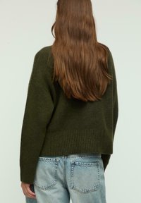 Maglione verde a maglia con una vestibilità comoda, orlo a coste e spalle basse, abbinato a jeans in denim chiaro.