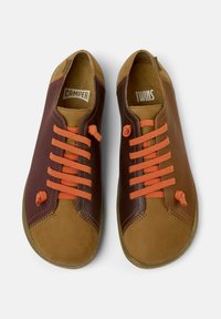 Sneaker in pelle marrone con lacci arancioni. Presenta un design bicolore: marrone scuro da un lato, beige dall'altro. Cuciture evidenti e suola in gomma.