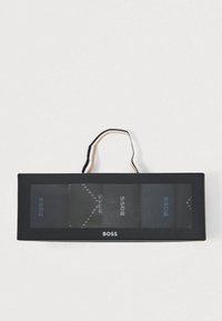 Σετ τριών σκούρων κάλτσες σε κουτί, με διαφανή μπροστινή πλευρά, μαύρη χαρτονένια συσκευασία και μαύρη και χρυσή λαβή.