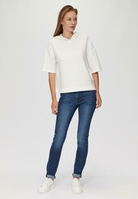 Un hoodie blanc à capuche avec un design texturé et côtelé, associé à un jean fitted bleu foncé et des baskets blanches, créant une tenue décontractée.