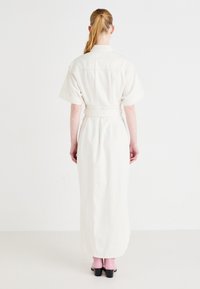 Kermanvärinen vyöllinen mekko, jossa on lyhyet hihat, suora leikkaus ja polvimittainen pituus. Mekossa on takakappale ja sileä rakenne.