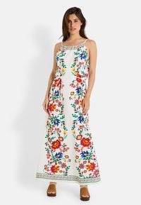 Vestido maxi de tela blanca con bordado floral colorido. Presenta tirantes finos, una cintura ajustable con cordón y un patrón decorativo en el dobladillo.