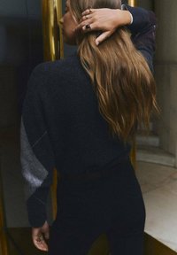 Maglione grigio scuro con dettagli grigio chiaro, caratterizzato da una vestibilità comoda e maniche lunghe. Il modello ha capelli lunghi e mossi e li tiene indietro.