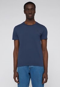 Námořnická modrá tričko s krátkým rukávem vyrobené z měkké bavlny, se klasickým krkem a malým logem na hrudi.