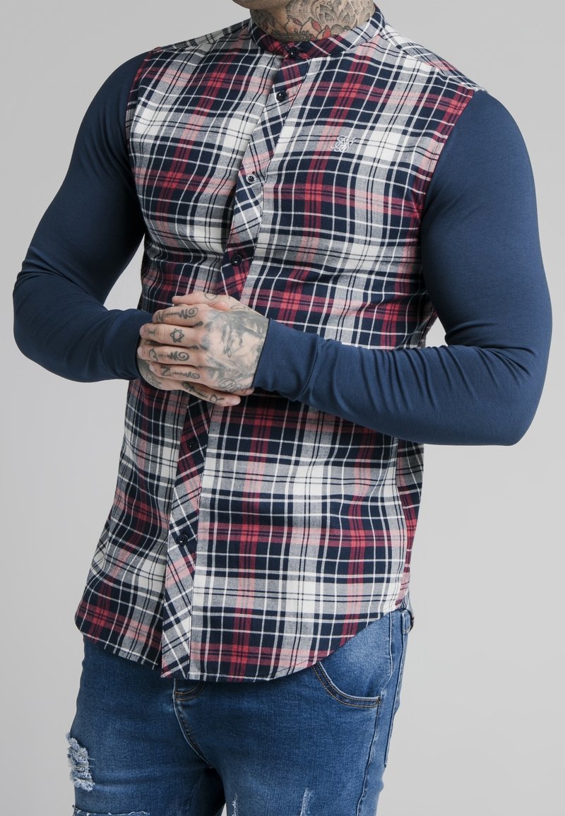 Button-up shirt with a red, navy, and white plaid pattern on the front and long navy sleeves. Features a collar and button closure.