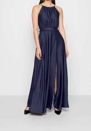 Granatowa satynowa sukienka bez rękawów z wysokim dekoltem, marszczonym taliowaniem, bocznym rozcięciem, noszona z czarnymi szpilkami na neutralnym tle.