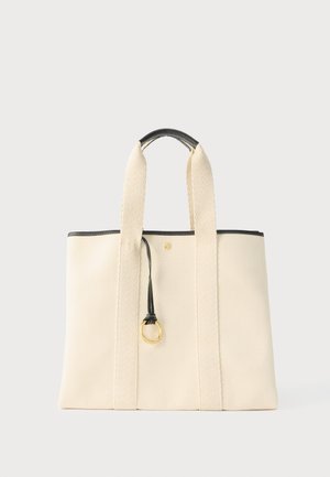 Sac fourre-tout en toile crème avec larges anses, poignée à bord noir et détail d'anneau doré suspendu au centre avant.