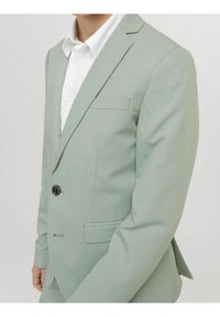 Jasnozielona marynarka o slim fit, zapinana na jeden guzik, z klapami i kieszenią na piersi. Materiał wydaje się gładki i dopasowany.