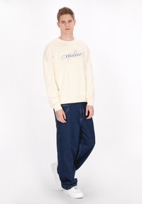 Felpa color crema con grafica "endless", abbinata a jeans blu scuro a vestibilità ampia e sneakers bianche. Tessuto morbido in tutto.