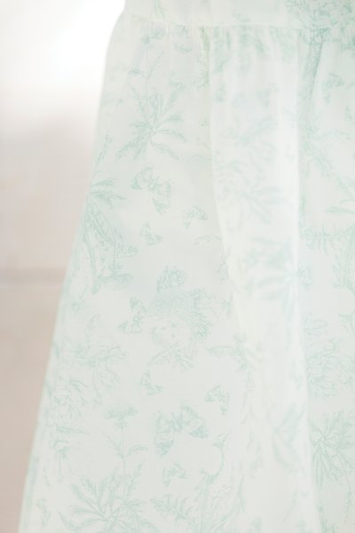 Tecido com padrão floral em verde menta suave e branco, apresentando delicados desenhos de folhas e borboletas. Textura leve e suave.