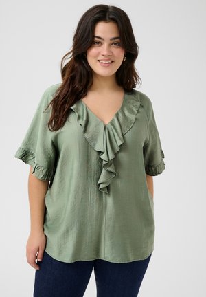 Blouse verte à manches courtes avec un décolleté en V profond et un détail froncé à l'avant. Textile texturé et manches volantes. À assortir avec un jean foncé.